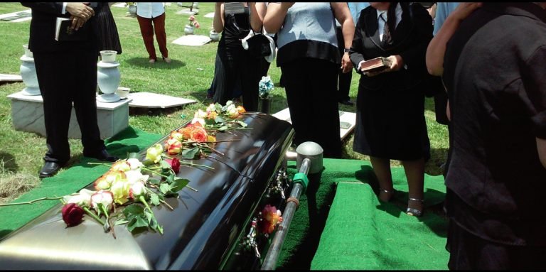 casket being lowered into a grave with flowers on top